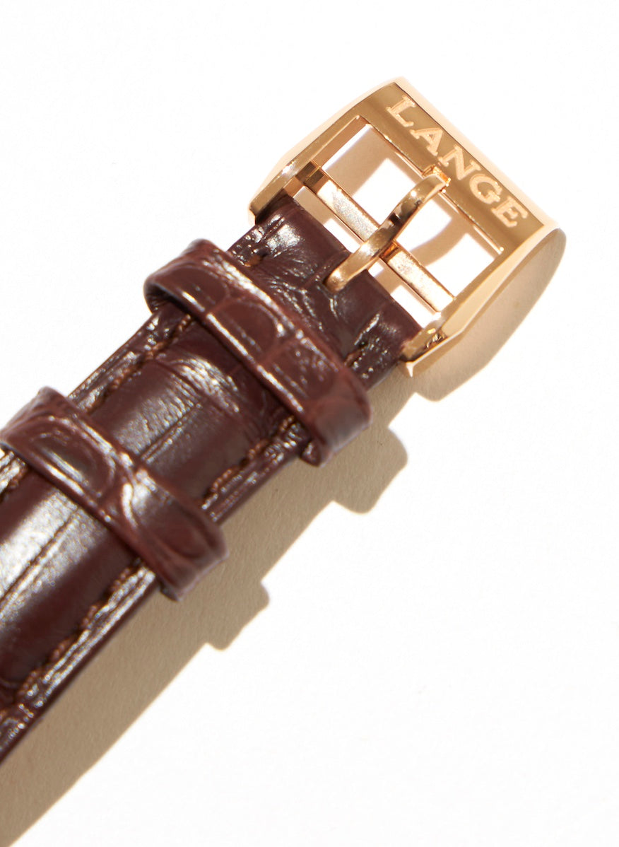 The hand-sewn, reddish brown alligator strap is fitted with a pink gold buckle engraved with the word 