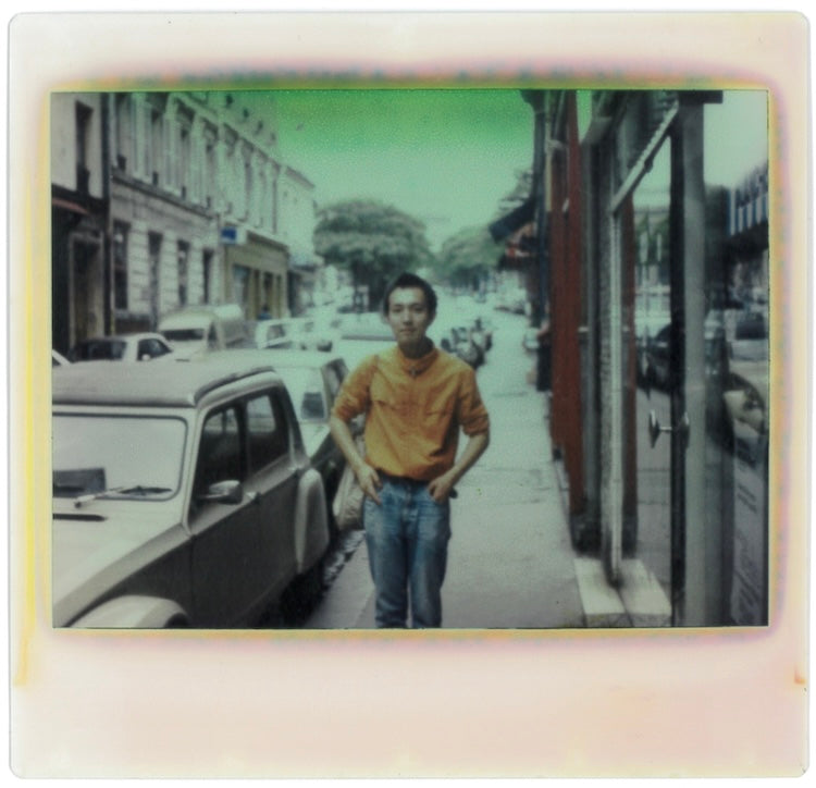 In 1981, he went to Spain, his first destination. He cut his hair short to save money before heading there. Pictured next to Shimazu is a Citroën 2CV, a car that represents France.