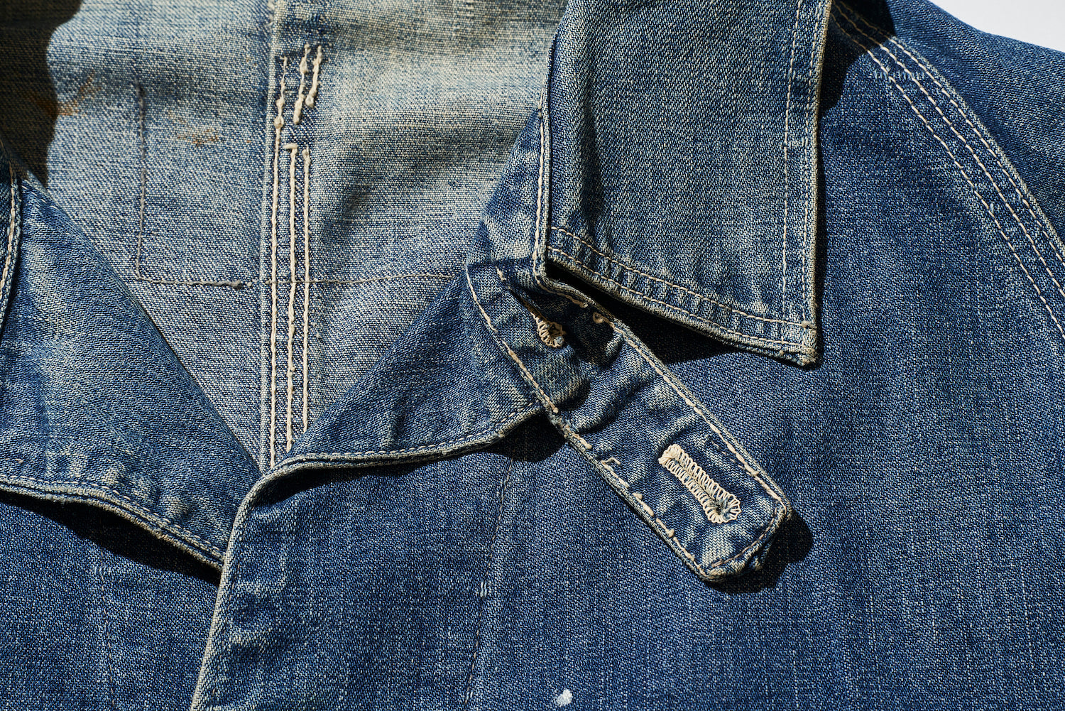 The strap attached to the top button was originally devised and adopted to accommodate shrinkage of the fabric.